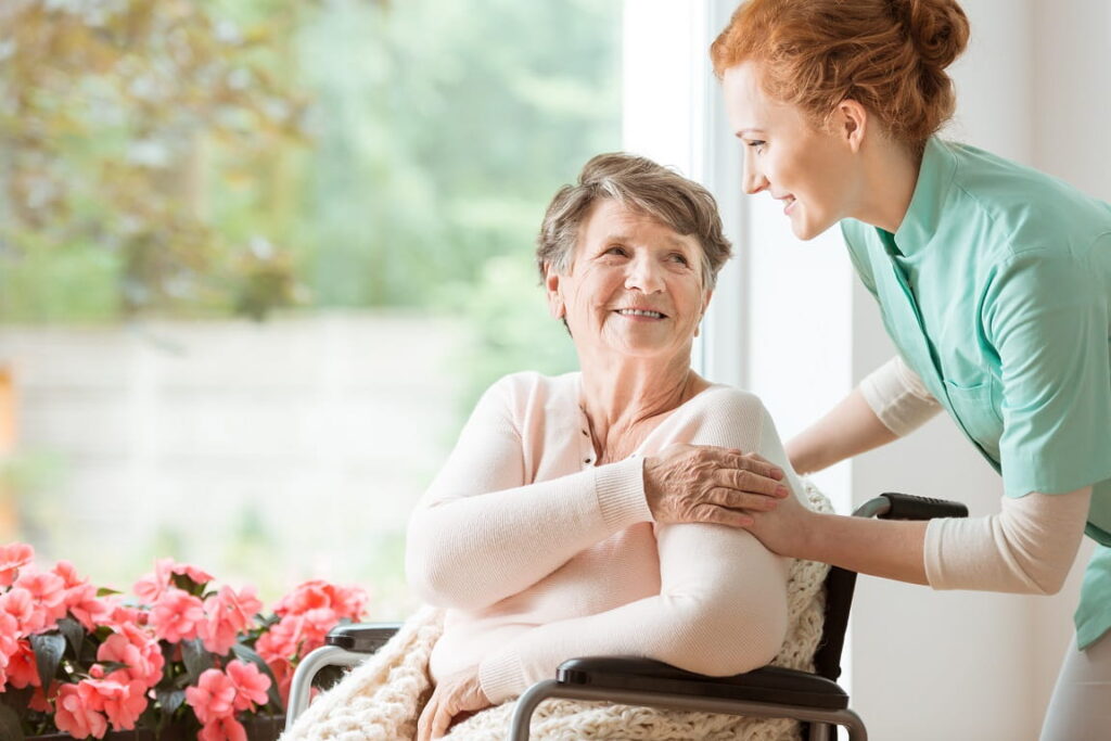 Pflegekraft hält die Hand älterer Dame im Rollstuhl