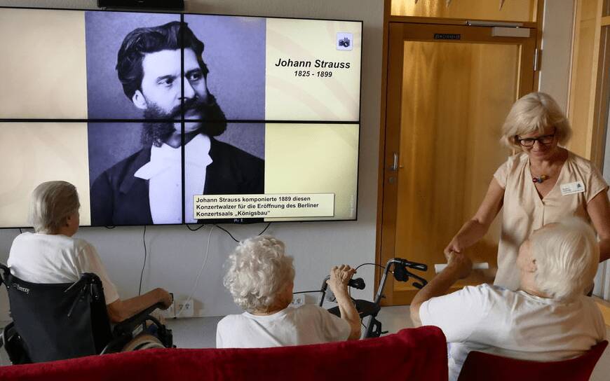 Biografiearbeit mit Technik: Bewohner und Betreuerin schauen sich Komponisten auf einer multimedialen Leinwand an.